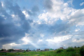 Obraz premium rural landscape. The sun's rays make their way through the clouds and Shine on the house after a thunderstorm