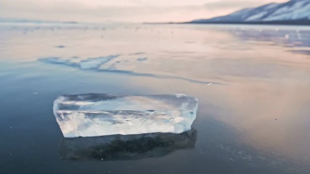 The ice floe rotates on the ice against the background of the amazing mountain landscape. Slow motion. The camera moves behind the ice. A piece of ice is very beautifully spinning on icy with magical
