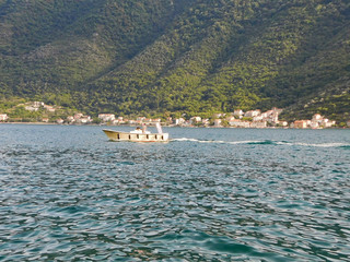 A boat speeding along the waves, in the background a green hillock in the Bay of Kotor