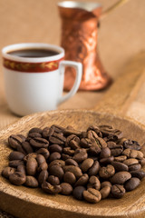 Roasted coffee beans in wooden ladle and traditional bronze coffee pot and cup on sackcloth