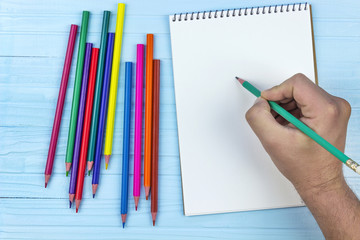 man begins to draw in a notebook for drawing, colored pencils, on a wooden blue background