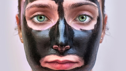 young adult woman with black skin care mask close up blue eyes indoors
