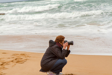 Woman Squatting and Photographing with a DSLR on the Beach