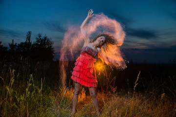 Obraz premium A girl in a black top and red skirt with white cloud arround her hair in a field during photoshoot with flour in sunset