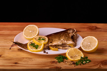 Appetizing baked fish, covered with juicy lemons, garlic and salt on side, above view