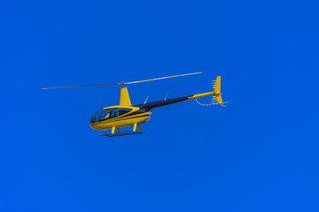 Yellow private helicopter in flight against the background of a bright blue sky with the participation of a crew member, shooting events below. Association with the national flag of Ukraine.