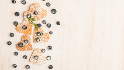 Traditional belgian waffles form of heart with fresh blueberry and sweet cherry on white wooden background. Flat lay, top view, copy space.