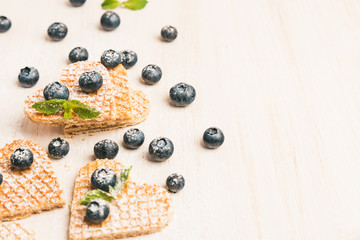 Traditional belgian waffles form of heart with fresh blueberry and sweet cherry on white wooden background. Flat lay, top view, copy space.