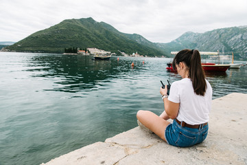 young adult woman sitting on pier with beautiful view of sea nd mountains. drone controller