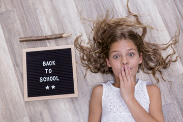 Cute smiling schoolgirl lying on the floor with letter board and smiling. Back to school concept....
