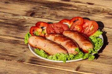 Grilled sausages with fresh vegetables on wooden table