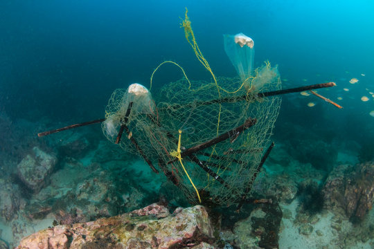 An abandoned ghost fishing net entangled on a murky, damaged tropical coral reef in Myanmar