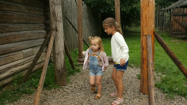 Children swinging on the wooden swing set. Two little girls walk and play outdoors in village. Kid's vacation