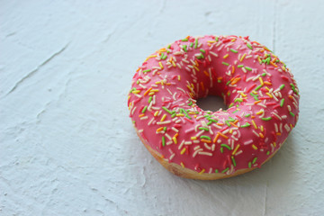Pink donut with multi-colored sprinkleson white textured background , top viewn. Free space for textn