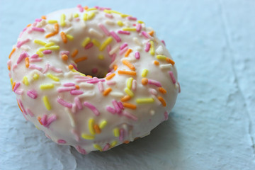 Donut in white glaze with multi-colored sprinkles on blue textured background close-up, top view