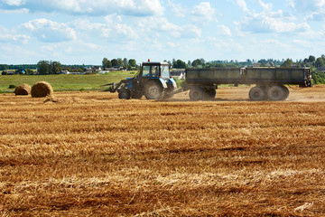 tractor removes haystacks in a field on a Sunny summer day
