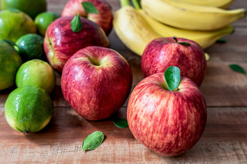 Colorful fresh bananas, lemons, oranges and apples on wooden background