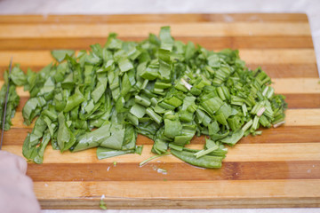 Woman cutting sorrel by knife on the wooden cooking desk