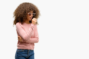 African american woman wearing pink sunglasses feeling unwell and coughing as symptom for cold or bronchitis. Healthcare concept.