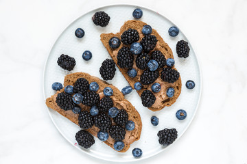 whole grain bread toasts with peanut butter, blueberries and blackberries on white marble table. healthy breakfast