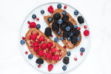 Healthy breakfast toasts for kids with peanut butter fresh berries and pomegranate seeds in a plate