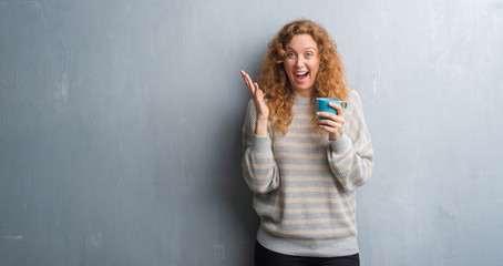 Young redhead woman over grey grunge wall drinking a cup of coffee very happy and excited, winner expression celebrating victory screaming with big smile and raised hands