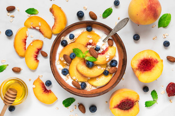 bowl of greek yogurt with peach, oats, nuts, mint, honey and blueberries with a spoon for healthy...