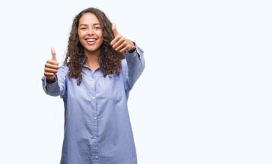 Young hispanic business woman approving doing positive gesture with hand, thumbs up smiling and happy for success. Looking at the camera, winner gesture.