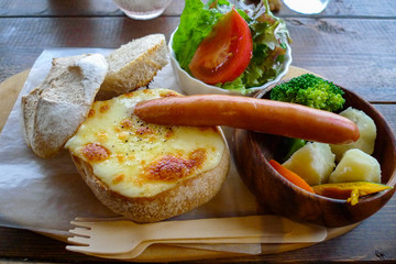 Cheese Fondue Bread Bowl with Sausage and Organic Warm Vegetable for dipping with Green Salad on wooden tray and fork, Rustic Cafe style. Perfect for picnic or backyard party during Autumn and Winter.