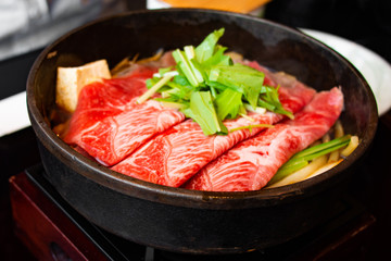 Tasty and delicious Japanese Sukiyaki nabe with best-quality cuts of thinly sliced sirloin or rib eye or tenderloin Kuroge Wagyu beef in a cast iron pan. Top and highest Marble Score. Natural light.