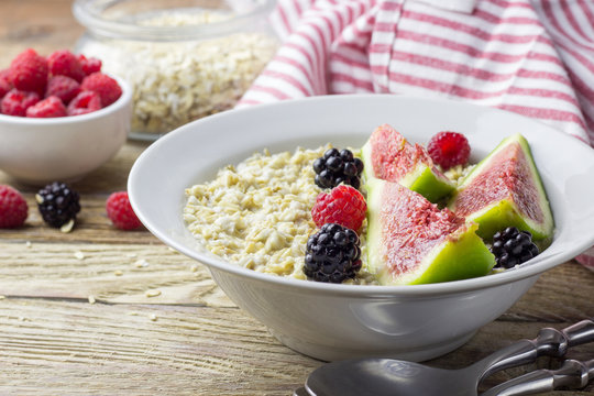Bowl of oatmeal porridge with figs, raspberries and blackberries on teal rustic table