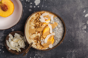 Smoothie bowl with chia pudding, peach, coconut and granola in a coconut bowl. Vegan healthy breakfast, clean eating concept.