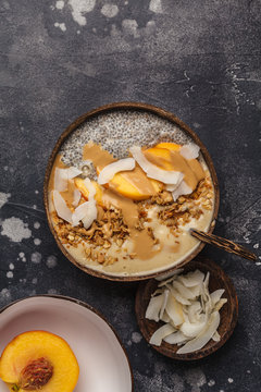Smoothie bowl with chia pudding, peach, coconut and granola in a coconut bowl. Vegan healthy breakfast, clean eating concept.