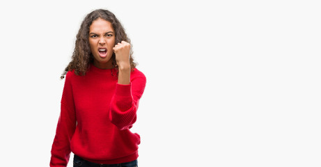 Obraz na płótnie Canvas Young hispanic woman wearing red sweater angry and mad raising fist frustrated and furious while shouting with anger. Rage and aggressive concept.