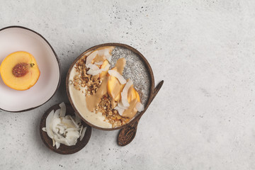 Smoothie bowl with chia pudding, peach, coconut and granola in a coconut bowl. Vegan healthy breakfast, clean eating concept.