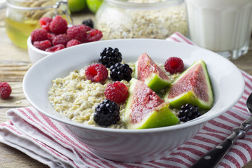 Bowl of oatmeal porridge with figs, raspberries and blackberries on teal rustic table