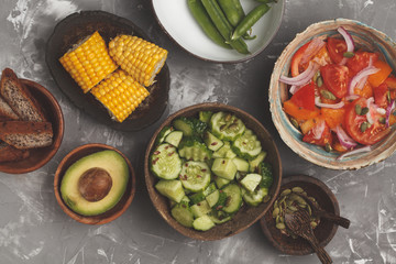 Clean eating concept. Cucumber salad, tomato salad, flax bread, avocado, corn. Top view, food background.