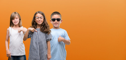 Group of boy and girls kids over orange background with surprise face pointing finger to himself