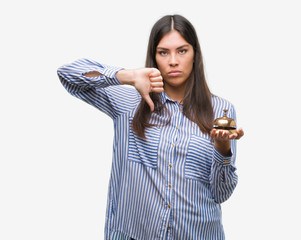 Young beautiful hispanic holding hotel ring bell with angry face, negative sign showing dislike with thumbs down, rejection concept