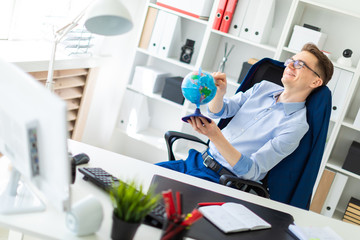 A young man sits in the office at the computer desk, closes his eyes and points a finger at the globe.