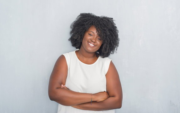 Young african american woman over grey grunge wall happy face smiling with crossed arms looking at the camera. Positive person.