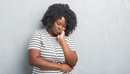 Fototapeta na wymiar Young african american plus size woman over grey grunge wall thinking looking tired and bored with depression problems with crossed arms.