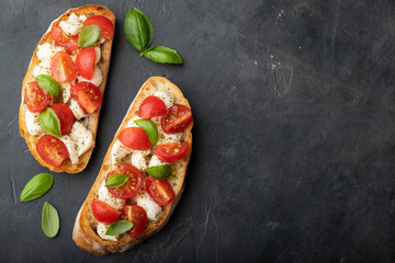 Bruschetta with tomatoes, mozzarella cheese and basil on a black background. Traditional italian appetizer or snack, antipasto. Top view with copy space. Flat lay