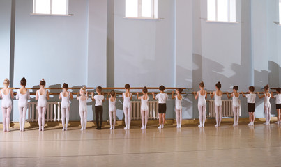 The training of young dancers in the ballet studio. Young dancers perform gymnastic exercises at the ballet or barre while warm-up in the classroom. © Evgeniy Kalinovskiy