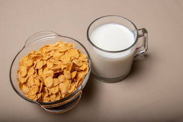 cornflakes in a glass plate a cup of milk on a gray background.