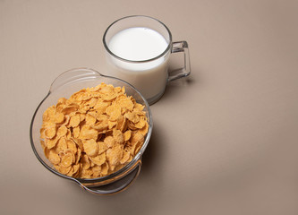 cornflakes in a glass plate a cup of milk on a gray background.