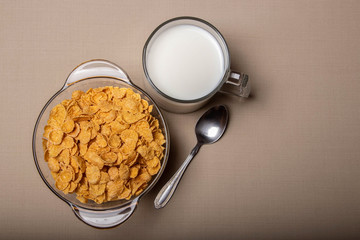 cornflakes in a glass plate a cup of milk on a gray background.