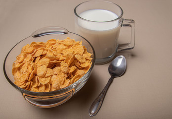cornflakes in a glass plate a cup of milk on a gray background.