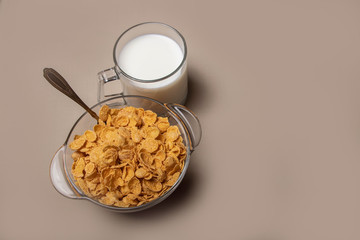 cornflakes in a glass plate a cup of milk on a gray background.
