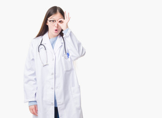 Young Chinese doctor woman over isolated background doing ok gesture shocked with surprised face, eye looking through fingers. Unbelieving expression.